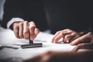 Close-up Of A Person’s Hand Stamping With Approved Stamp On Text Approved Document At Desk, Contract Form Paper Certificado de autenticidad